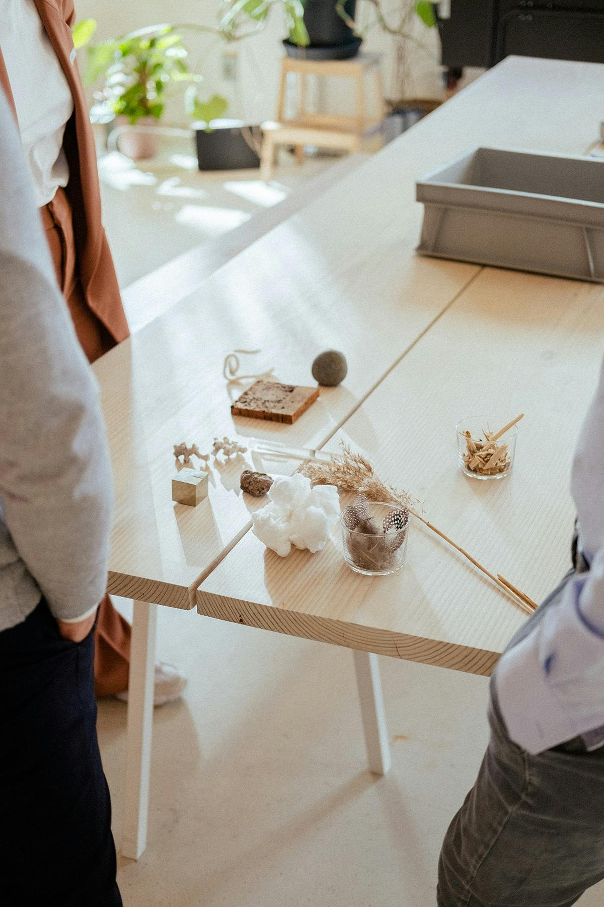 Different objects and materials on a table with people standing around
